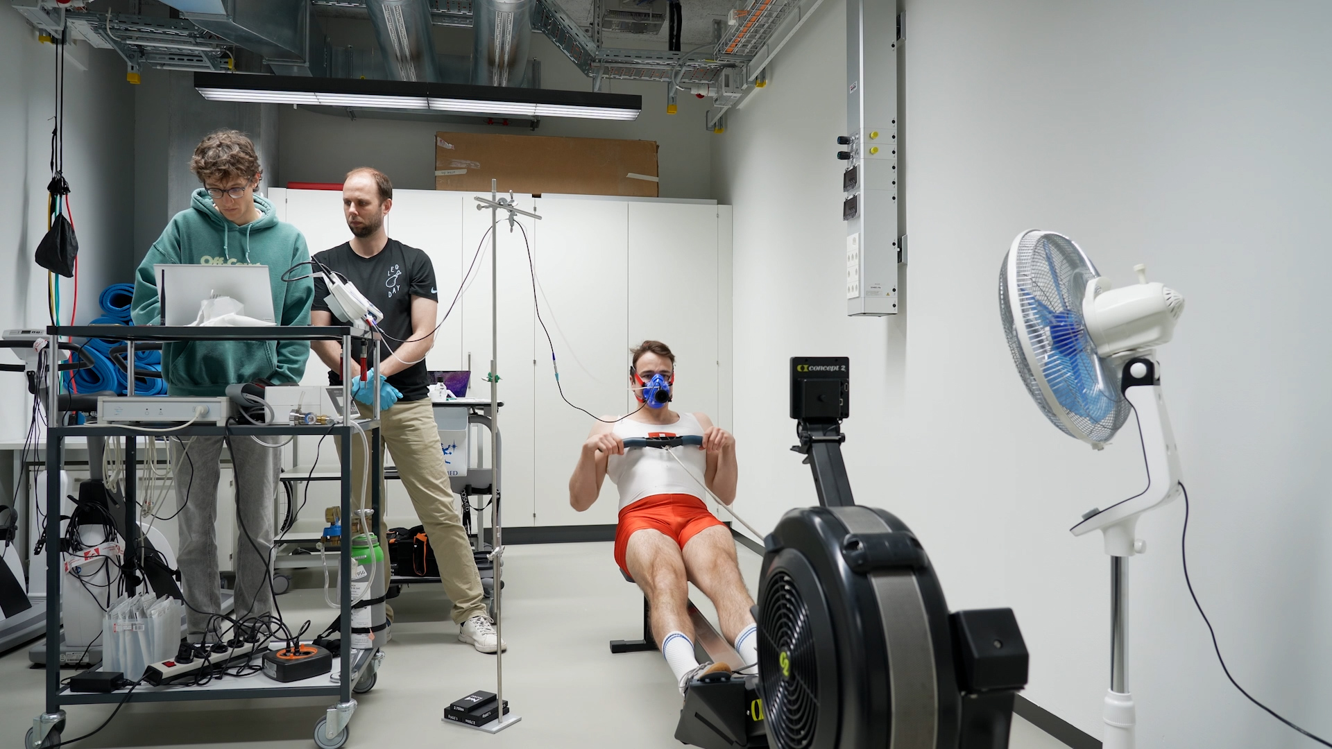 A man on the rowing machine is monitored by two people.