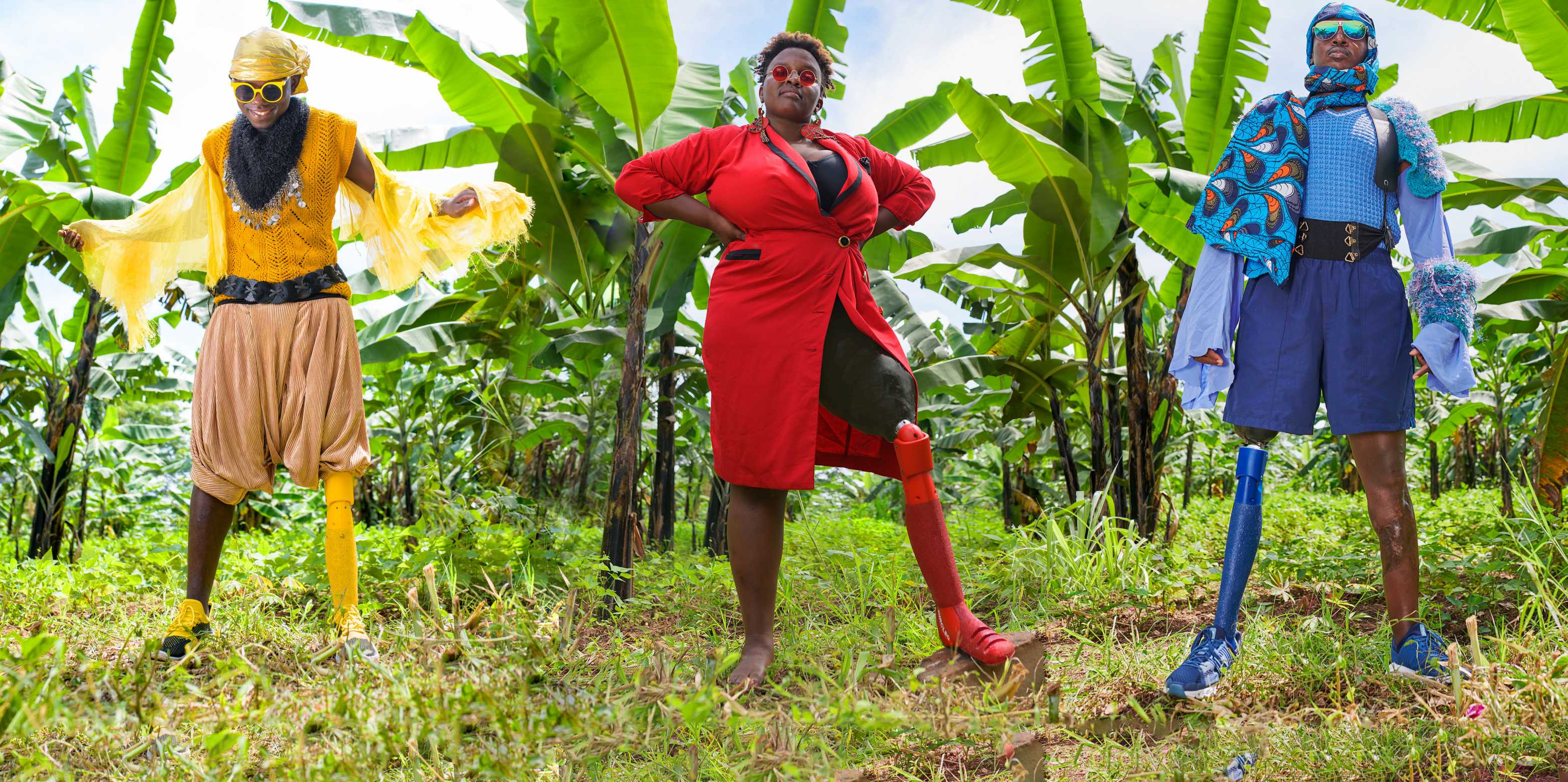 In a banana garden, three persons, colourfully dressed, each one of them with a leg prosthesis in a matching colour 
