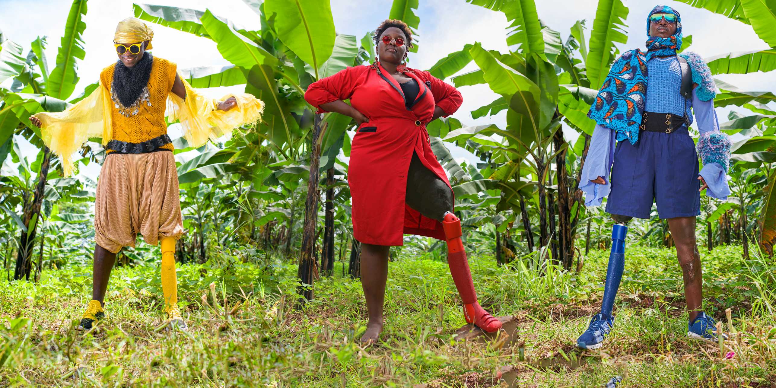 In a banana garden, three persons, colourfully dressed, each one of them with a leg prosthesis in a matching colour 