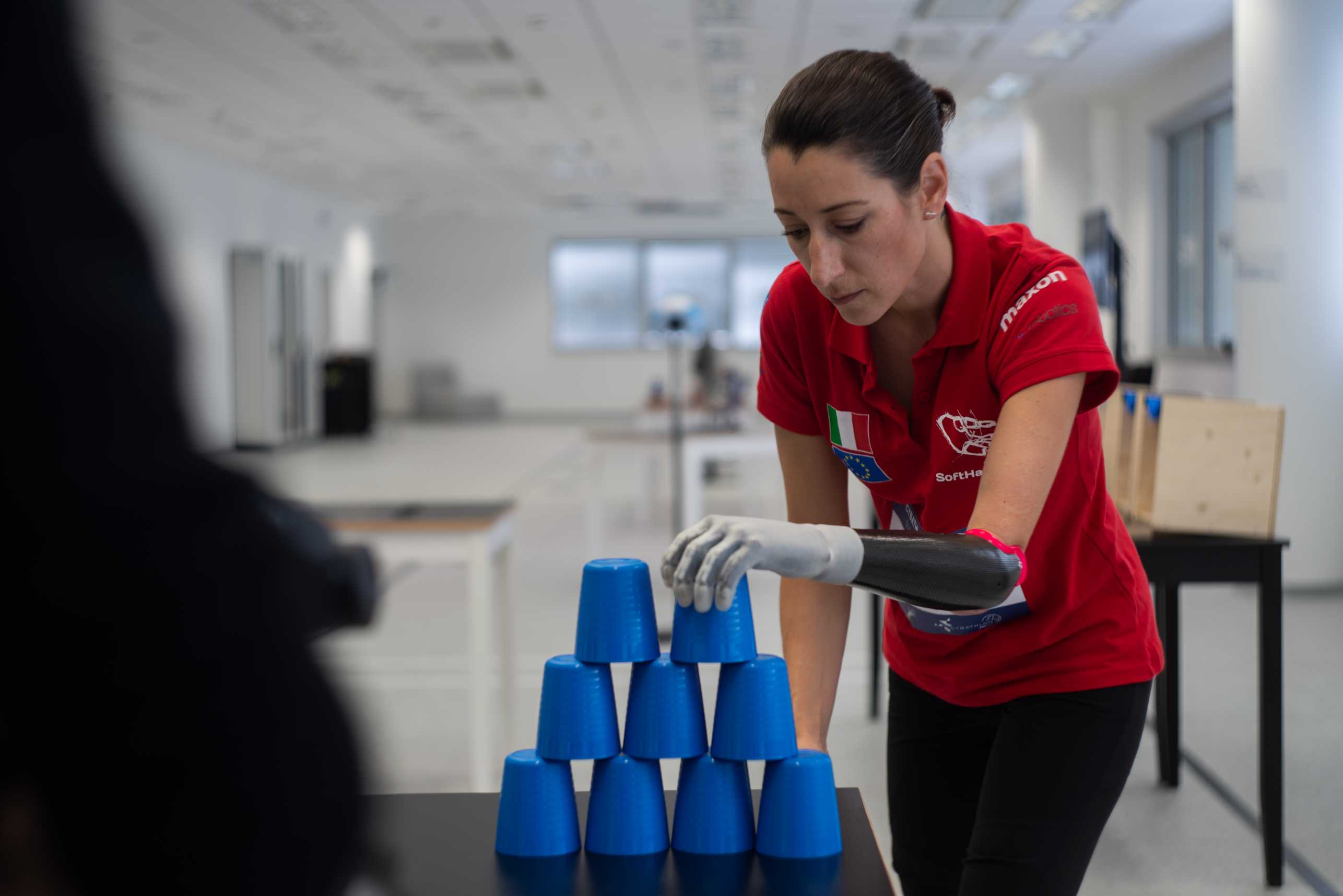 Maria Fossati, designer and researcher, using her prosthetic arm to make a pyramid of blue cups.