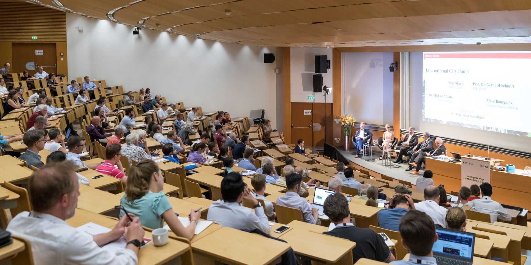 Das Bild zeigt einen Vorlesungssaal an der ETH, in dem zahlreiche Menschen sitzen und einer Podiumsdiskussion mit fünf Podiumsgästen zuhören.