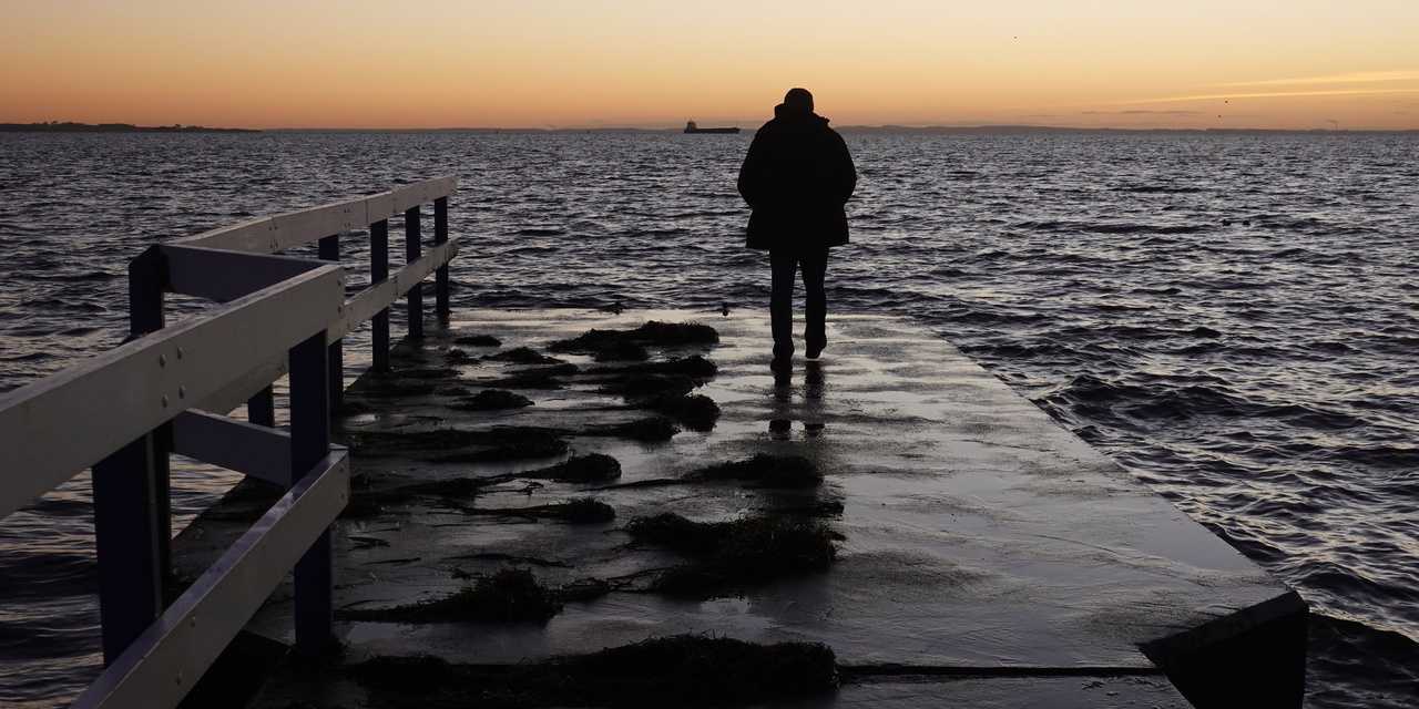 Mann steht auf einem Steg und schaut über das Wasser in den Sonnenuntergang.