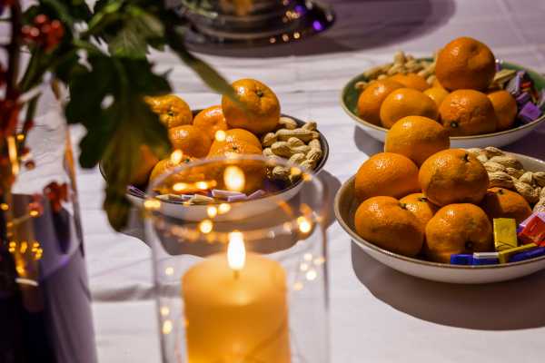 Tisch mit Teller voll Mandarinen und Nüssen und stimmungsvollen Kerzen.