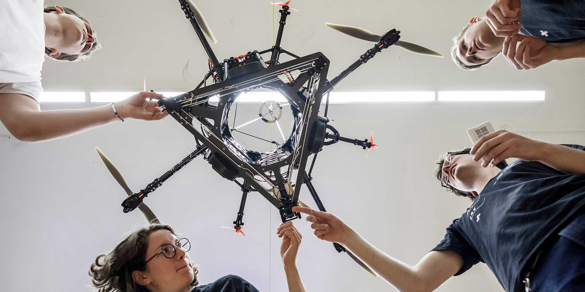 Studierende beugen sich über den Roboter "Spacehopper" und fassen ihn an. Das Bild wurde von unterhalb des Roboters aufgenommen