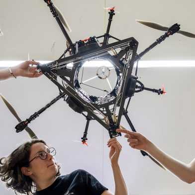 Studierende beugen sich über den Roboter "Spacehopper" und fassen ihn an. Das Bild wurde von unterhalb des Roboters aufgenommen