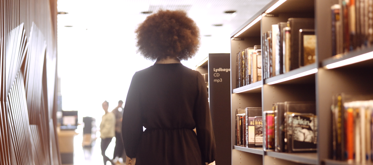 Person walking along bookshelfs in a library.