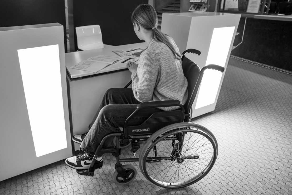 A woman in a wheelchair looks at paperwork at a barrier-free registration desk.