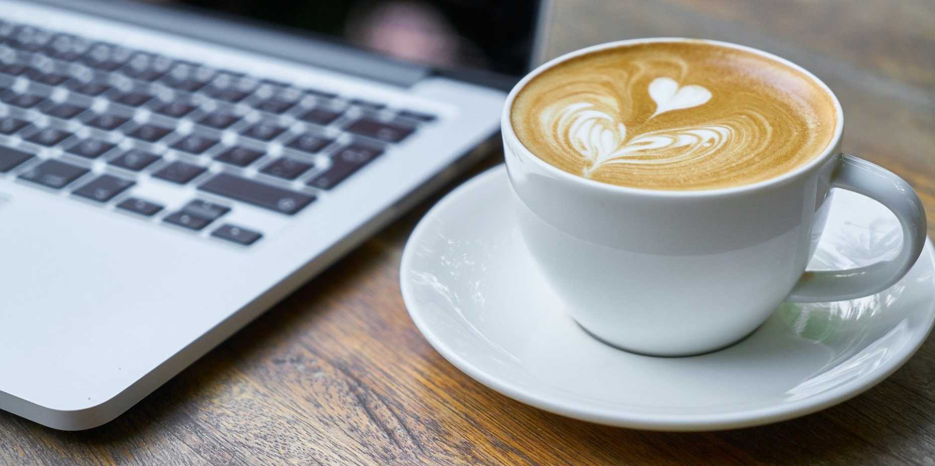 Kaffeetasse neben MacBook auf Holztisch