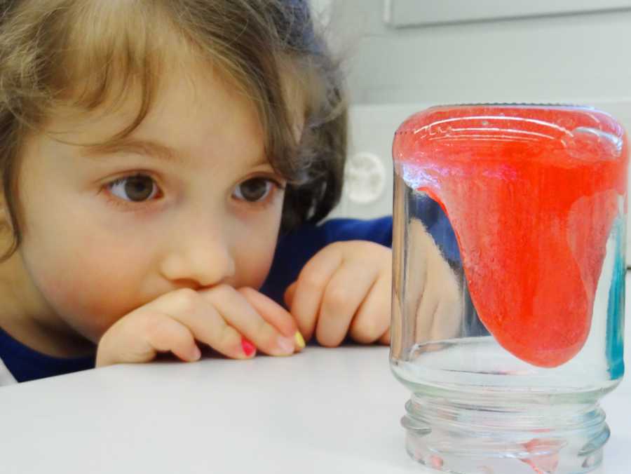 Girl observes a glass with red slime in it.