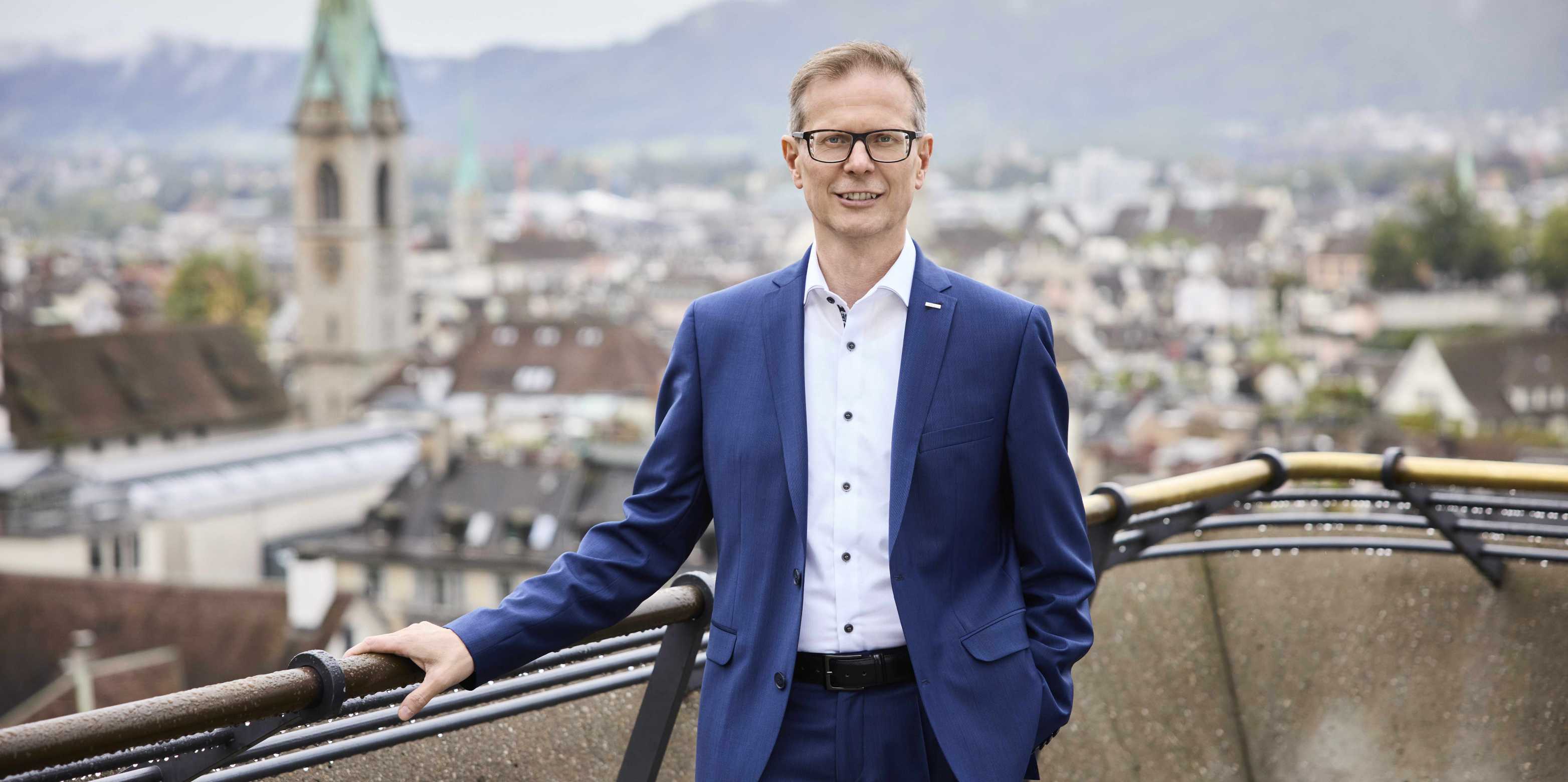 Rector Günther Dissertori wears a blue suit and stands on Polyterasse. The city of Zurich can be seen in the background.