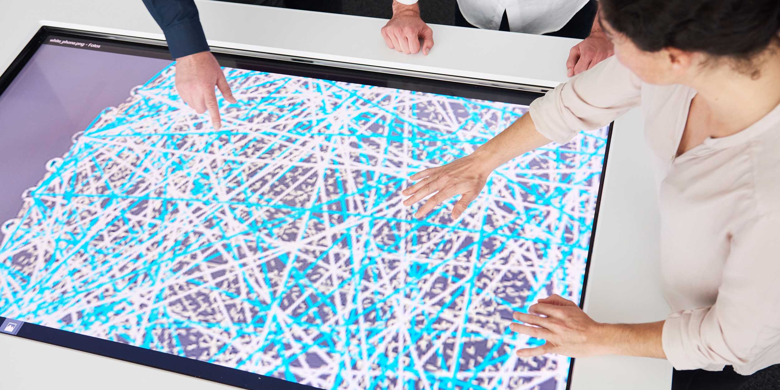 Two people point with their hands to a screen on which a network of white and blue lines can be seen.