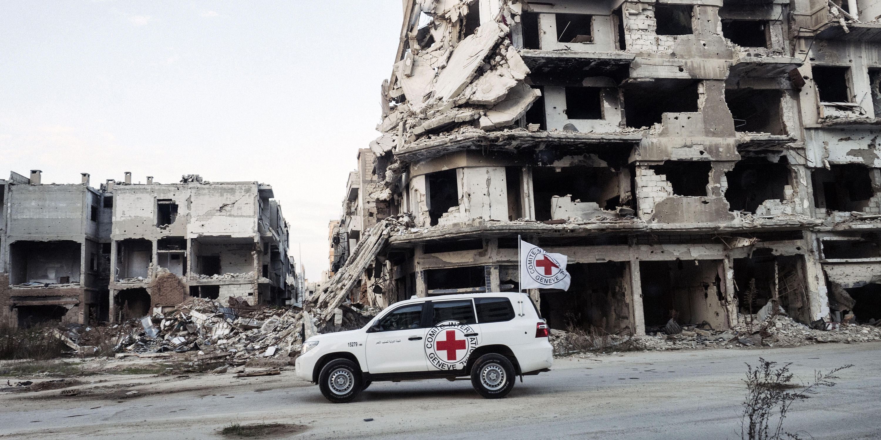 An ICRC car in front of a destroyed house facade