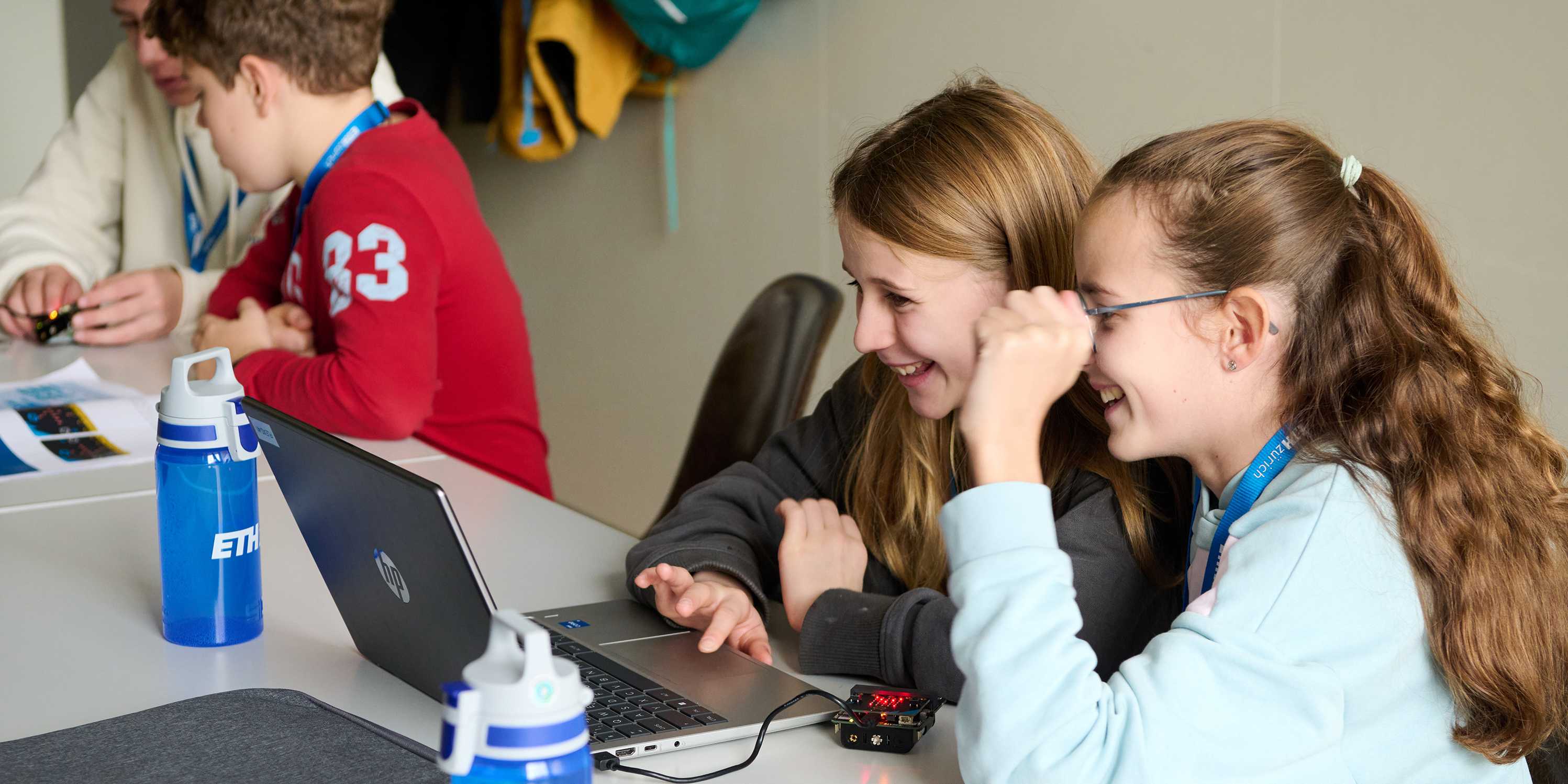 Two children are sitting at a computer and having fun.