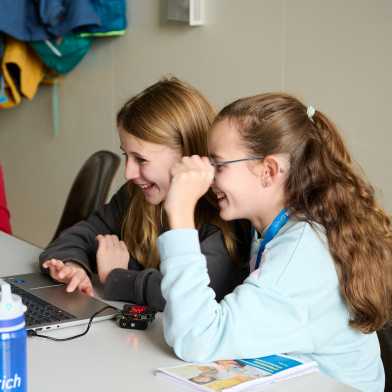 Two children are sitting at a computer and having fun.