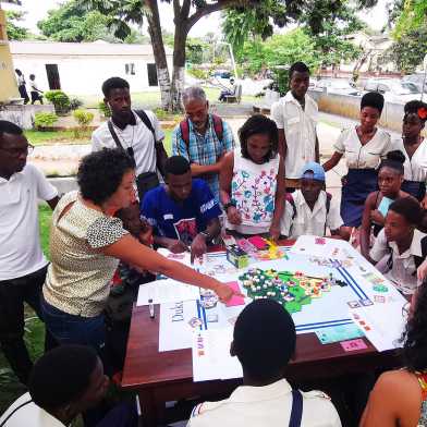 A woman points to a piece of paper on the table while other people listen and also look at the table